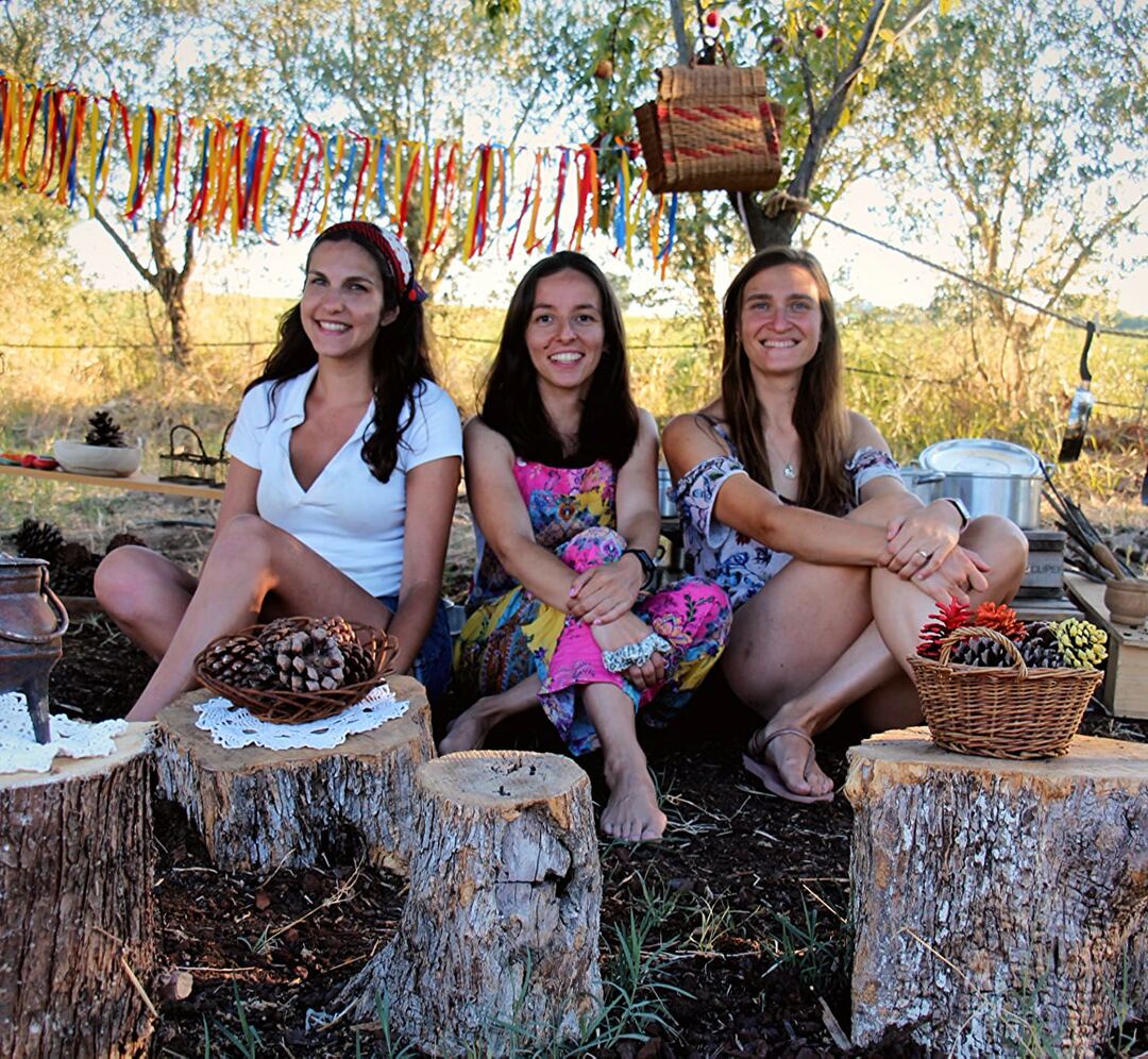 Joana Gradíssimo, Joana Oliveira e Rita Rosa, sentadas no campo, debaixo de um fio de fitas coloridas